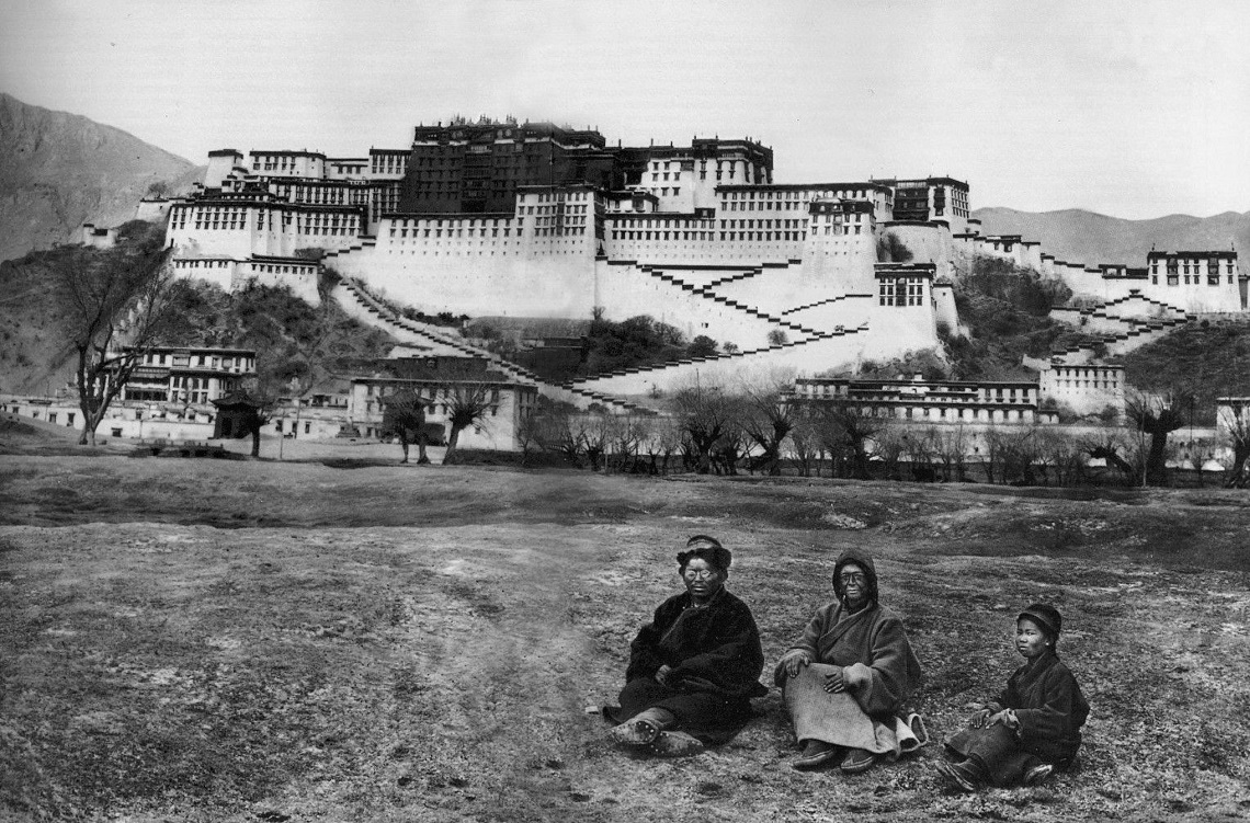 Alexandra in, dressed as a beggar and face covered in grease, Lama Yongden, and a young Tibetan pose upon the backdrop of the Potala Palace, in Lhasa, Tibet's capital, in 1924